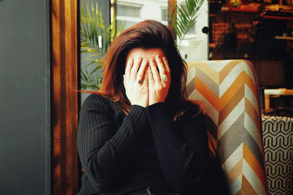 adult acne stigma. Why am I still spotty at 37? a woman hides her face in her hands.